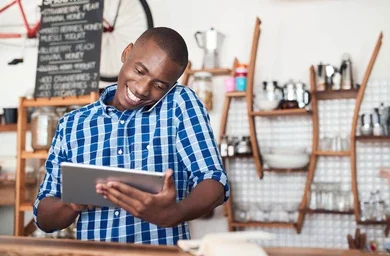 Smiling South African small business owner looking at hos laptop in a cafe, representing ease of use.